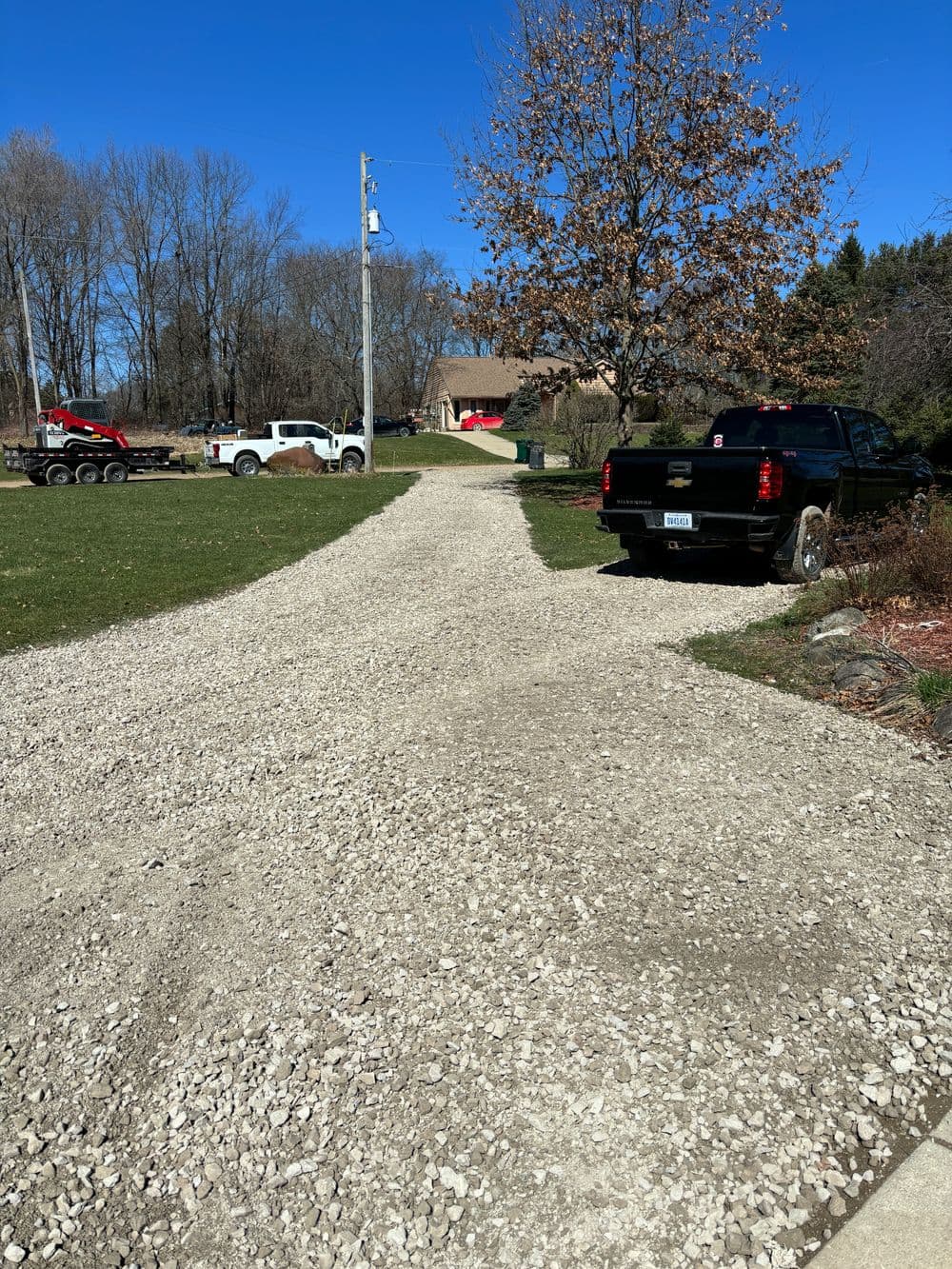 Gravel driveway with two trucks parked, leading to a house surrounded by trees.