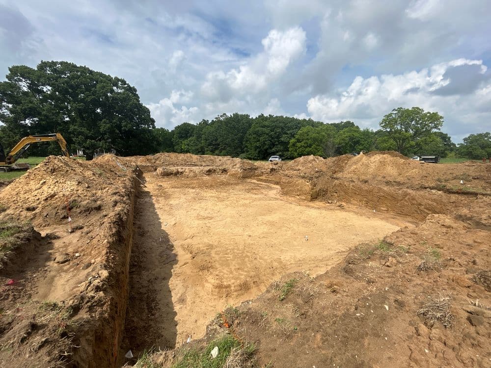 Excavated construction site with earth mounds and cloudy sky in the background.