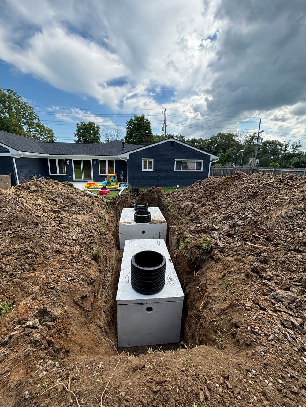 Two concrete retention tanks in a trench, with a house and playground visible in the background.