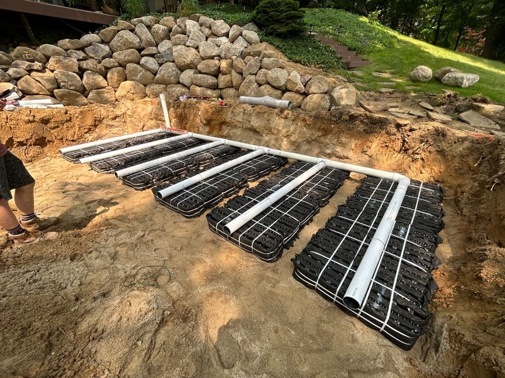 Installation of a drainage system with piping and gravel grid in a landscaped area.